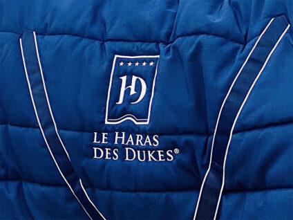 Logo brodé du Haras des Dukes sur une couverture équestre bleue, identité visuelle haut de gamme.